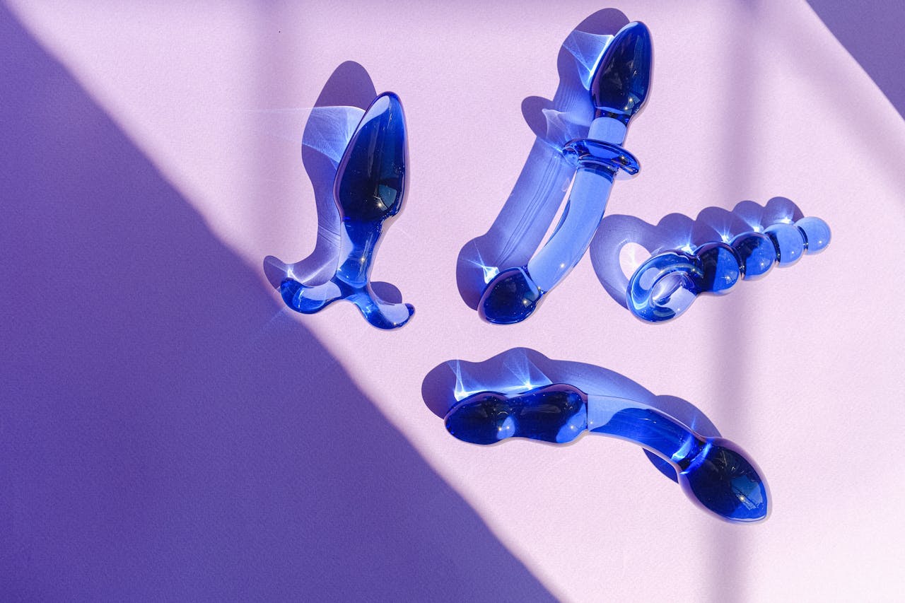 Artistic arrangement of blue glass adult toys on a purple backdrop, exuding elegance and modern style.